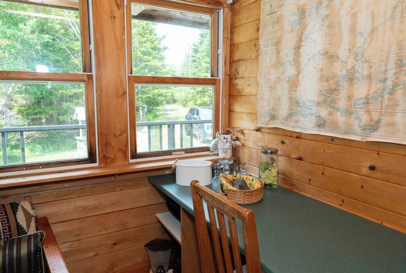 A cabin interior with wooden walls, a large window, a wooden bench, a chair, and a map on the wall.