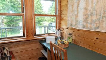 A cabin interior with wooden walls, a large window, a wooden bench, a chair, and a map on the wall.
