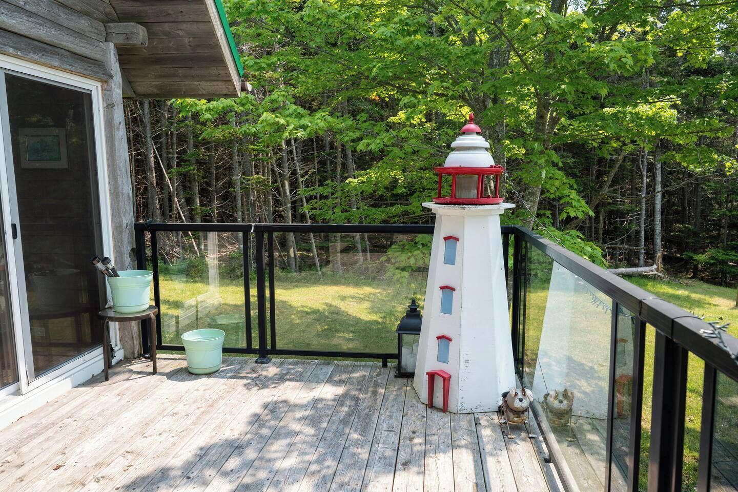 Une terrasse en bois agrémentée d’une maquette de phare blanc, d’une rambarde en métal et d’une porte en verre donnant sur un espace abrité.