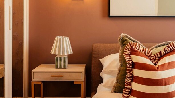 Habitación de hotel con una mesita de noche, una lámpara, una cama con almohadas a rayas y una lámpara de pared.