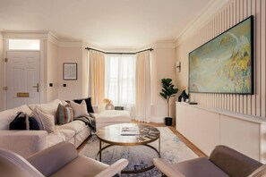 Ein Wohnzimmer mit einer Couch, Sesseln, einem Couchtisch und einem großen Gemälde an der Wand.