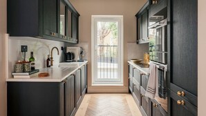 Una cocina con armarios oscuros, encimera blanca y vistas al balcón exterior a través de una puerta.