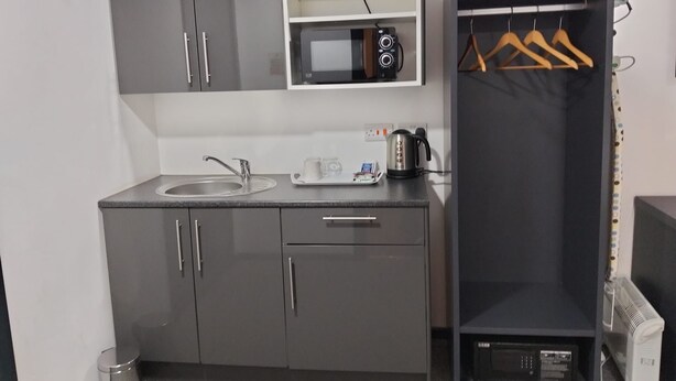 Una kitchenette compacta con microondas, pileta y una pequeña estantería.