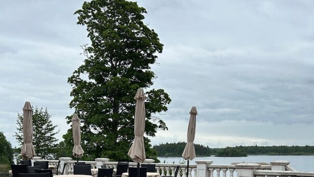 En uteservering med bord och stolar, parasoller och utsikt över en sjö.