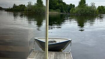 A wooden dock with a boat moored at the end, surrounded by calm water and trees.