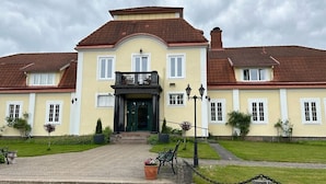 Ein großes Gebäude mit einer symmetrischen Fassade, einem zentralen Eingang mit einer grünen Tür und einer gepflasterten Auffahrt zu einer Bank.