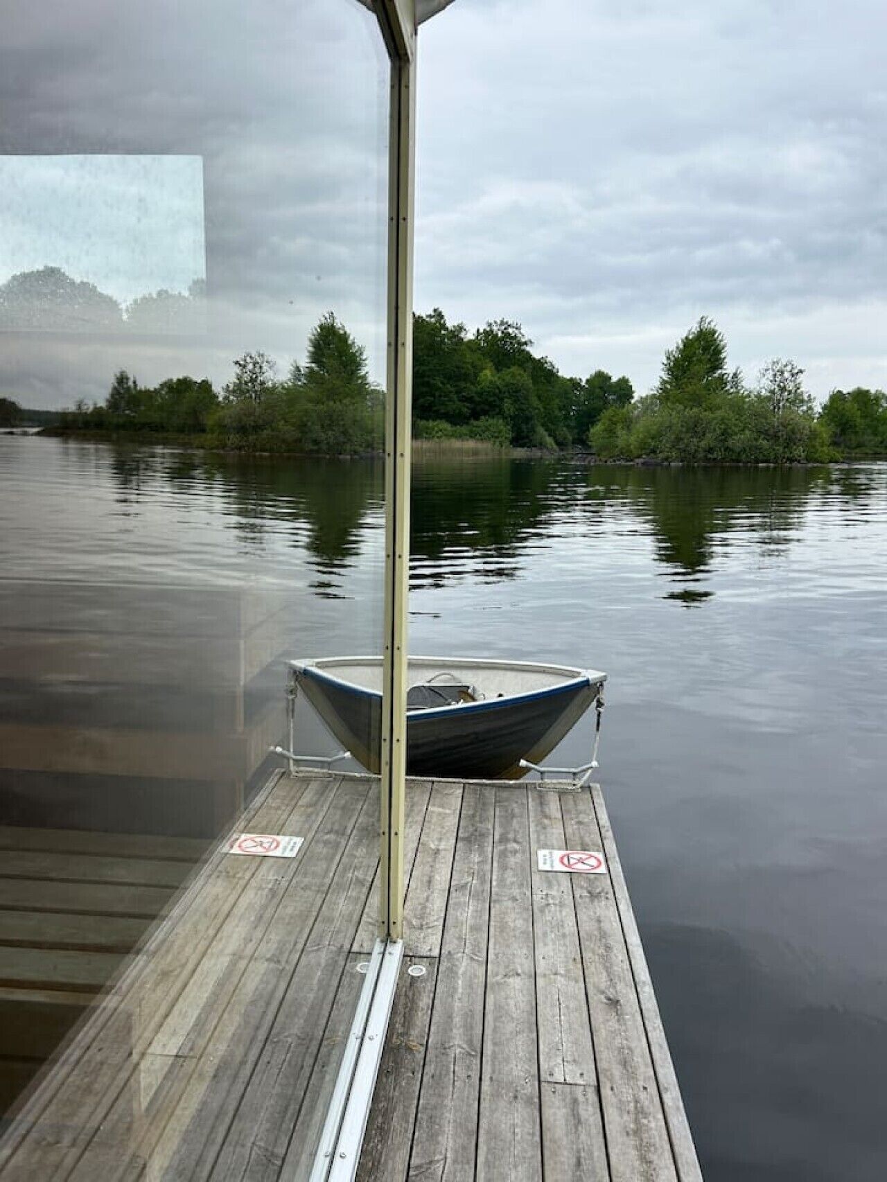 A wooden dock with a boat moored at the end, surrounded by calm water and trees.