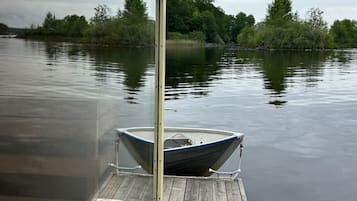 A wooden dock with a boat moored at the end, surrounded by calm water and trees.