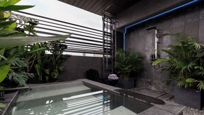 Een moderne badkamer met een glazen pool, een douchegedeelte met een blauw verlichte wand, en diverse planten.