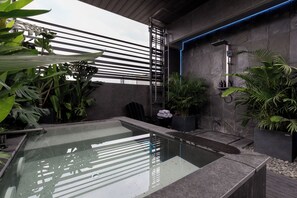 A modern bathroom with a glass-enclosed pool, a shower area with a blue-lit wall, and various plants. - Deep Blue Studio@Saigon's alley with Rooftop Onsen (Thành phố Hồ Chí Minh)