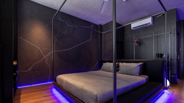 Een moderne slaapkamer met een bed met glazen scheidingswand, donkere wanden en een houten vloer.