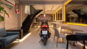 Een motorfiets staat in een moderne ruimte met een trap, een zithoek en een eettafel.