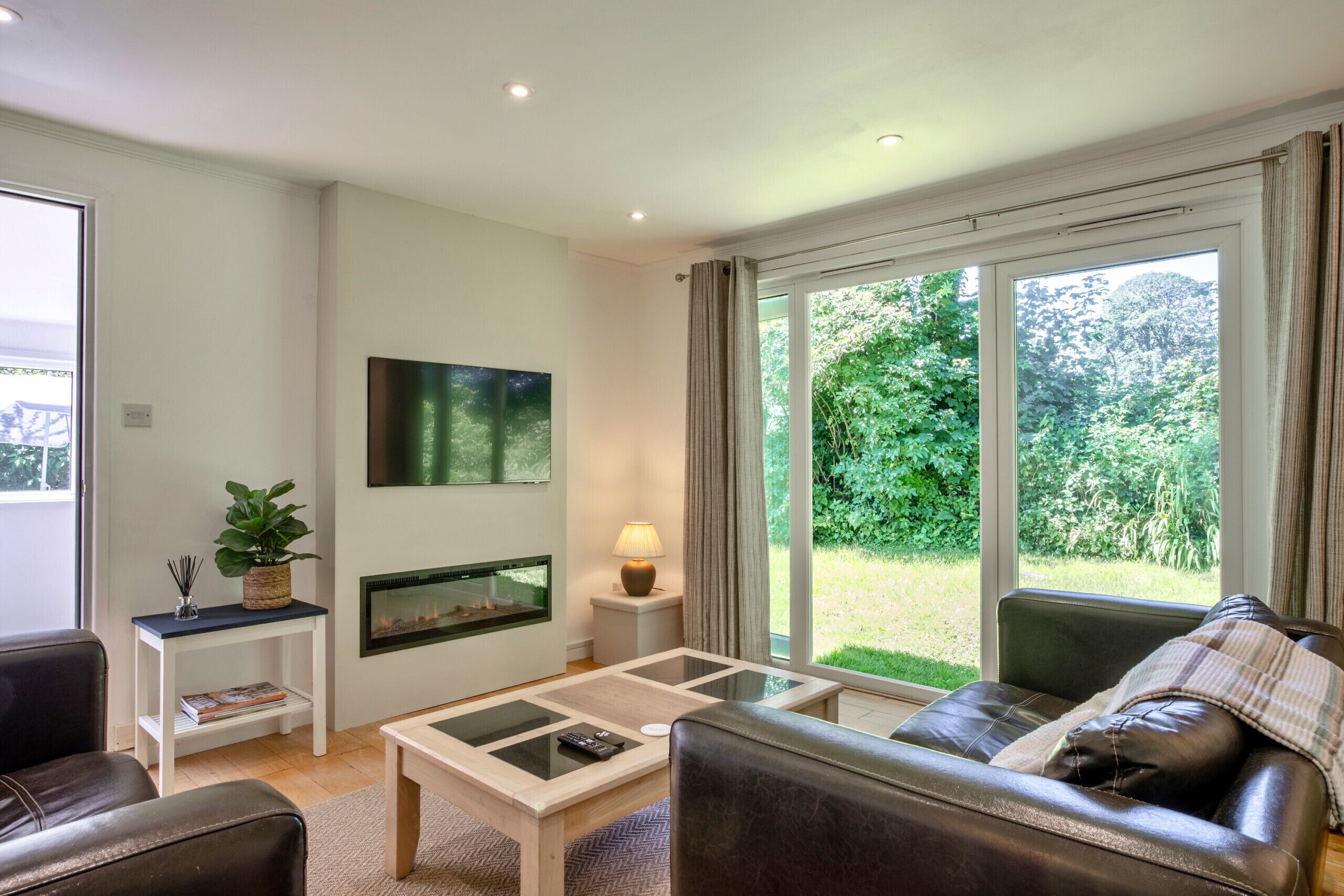 A living room with a sofa, coffee table, fireplace, and large windows with a view of greenery.
