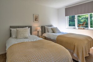 A double room with two beds, a bedside table with a lamp, a framed picture on the wall, and a window with a view of greenery and a horse statue. - Brockwood (Bradworthy)