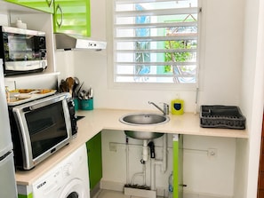 Eine kleine Küche mit Waschmaschine, Mikrowelle, Spüle und einem Fenster mit Jalousien.