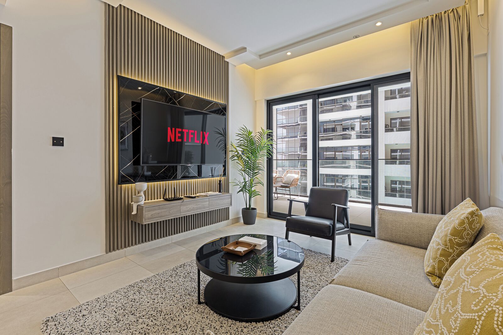 A modern living room with a large flat-screen TV, a sofa, a coffee table, and a potted plant.
