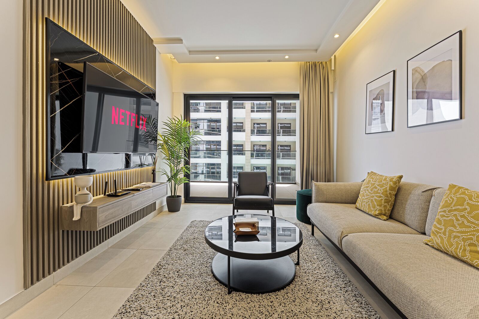 A modern living room with a flat-screen TV, a sofa, a coffee table, and a potted plant.