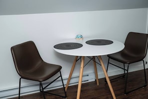 A small round table with two brown chairs, a white wall, and a wooden floor.