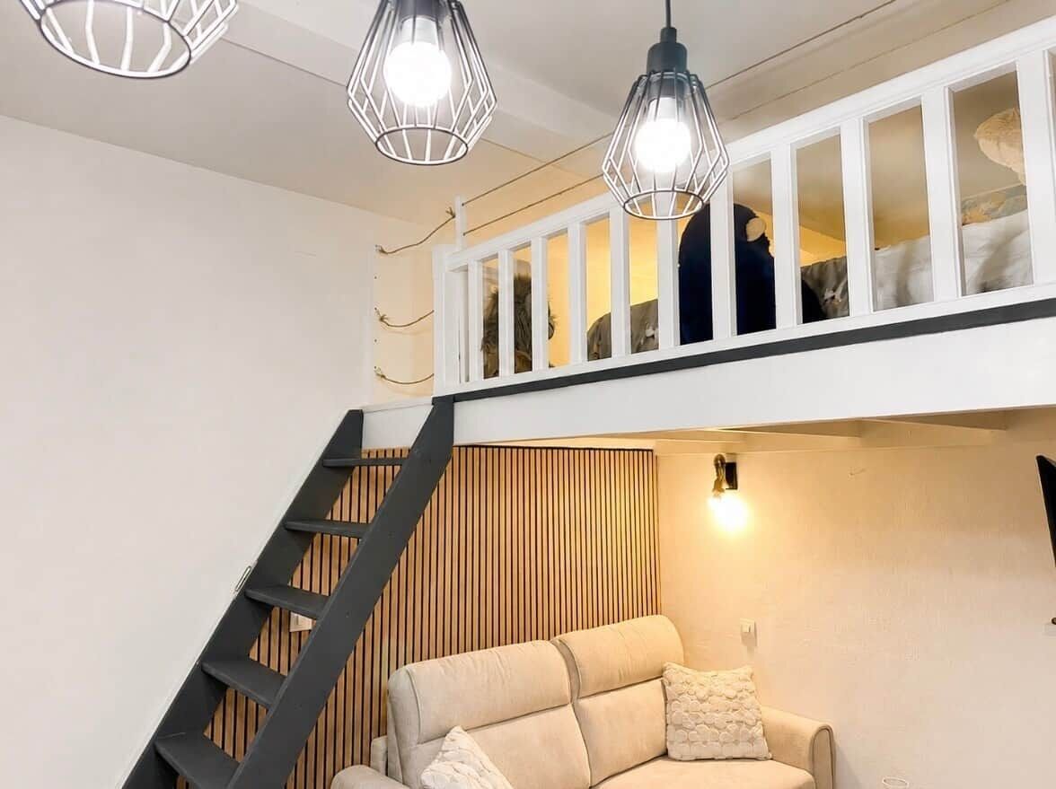 A loft-style room with a staircase, a sofa, and a cat on the upper level.