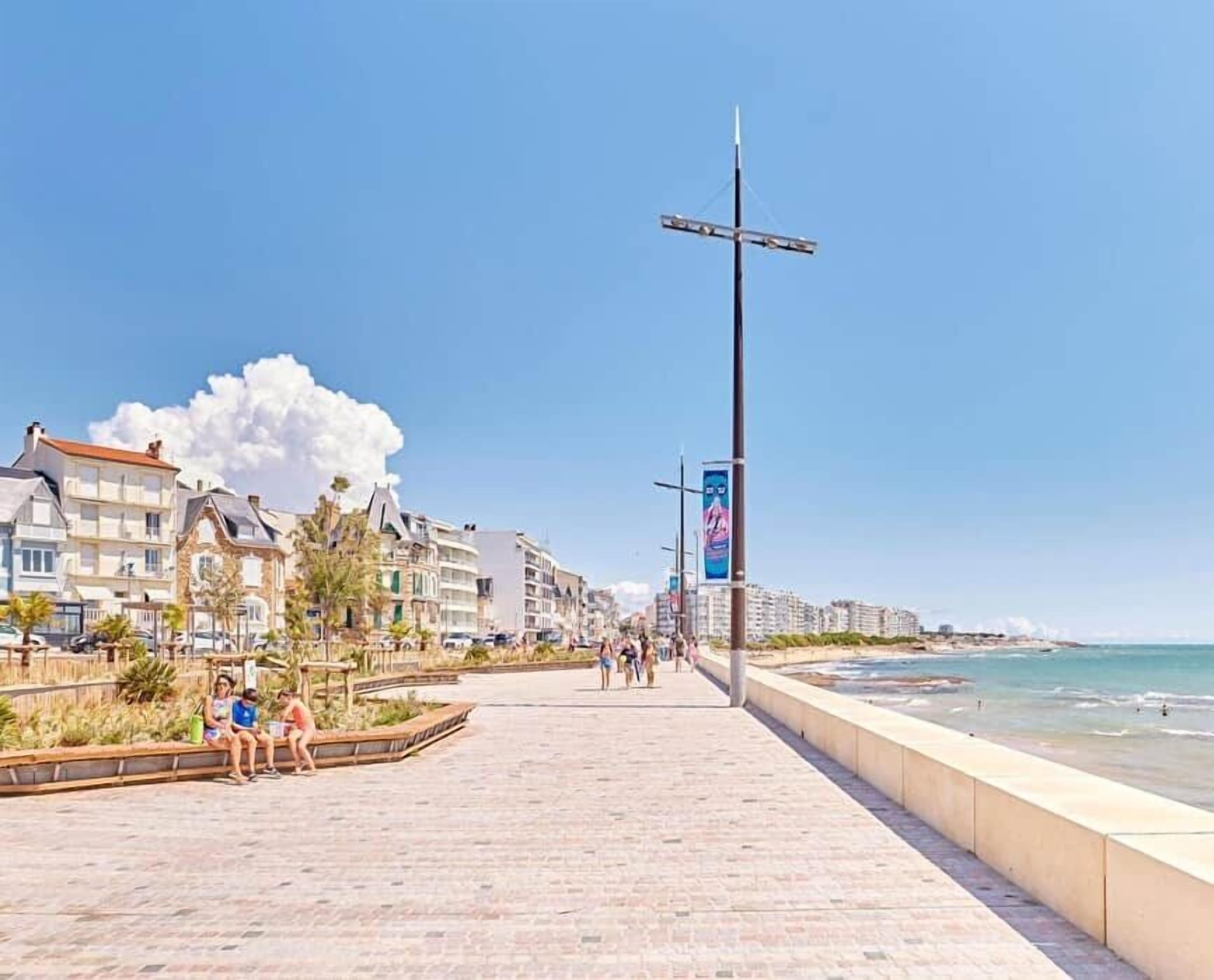 Un chemin pavé longe la plage, avec des bâtiments d’un côté et l’océan de l’autre.