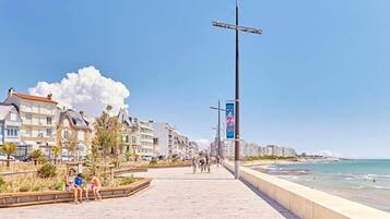 Un chemin pavé longe la plage, avec des bâtiments d’un côté et l’océan de l’autre.