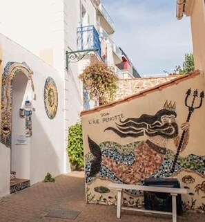 Un callejón estrecho con un mural en un edificio, una mesa pequeña y una planta colgante.