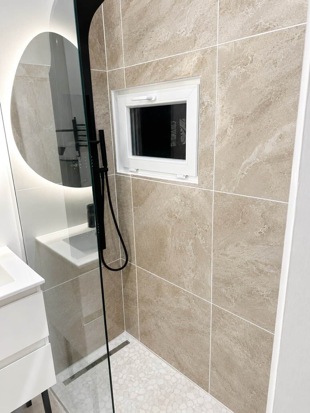 Une salle de bain moderne avec une douche à parois de verre, une petite fenêtre et un mur recouvert de carreaux de marbre.