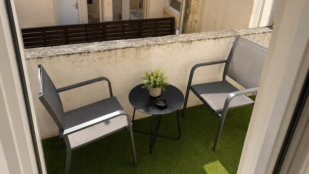 Een balkon met twee stoelen, een kleintje tafeltje en een potplant.