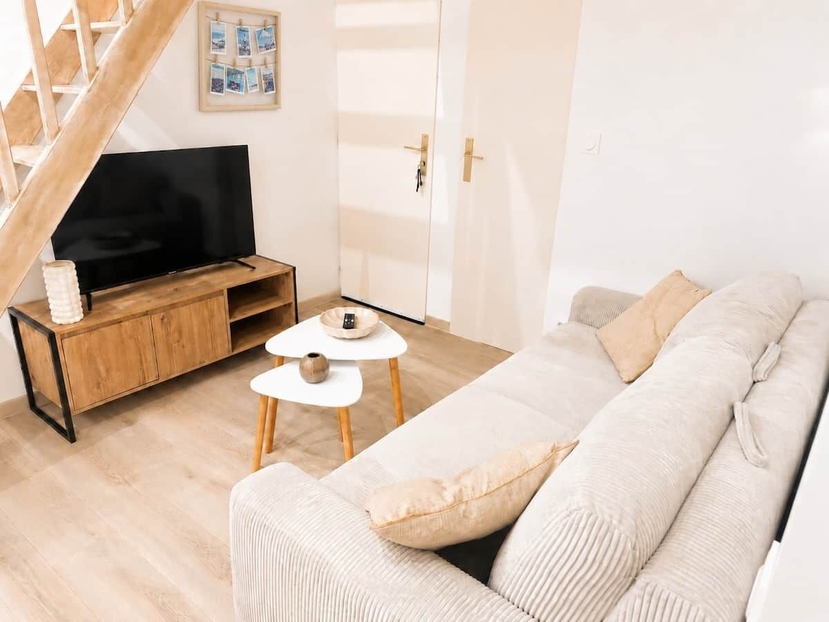 Ein Wohnzimmer mit einer Couch, einem Couchtisch, einem Fernseher auf einem Holzboden, einer Treppe und einer Tür mit Lichtschalter.