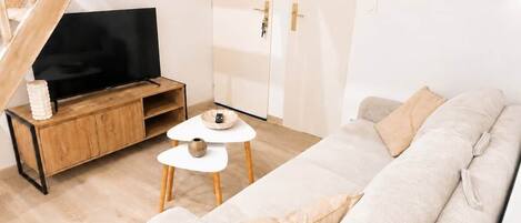 Ein Wohnzimmer mit einer Couch, einem Couchtisch, einem Fernseher auf einem Holzboden, einer Treppe und einer Tür mit Lichtschalter.