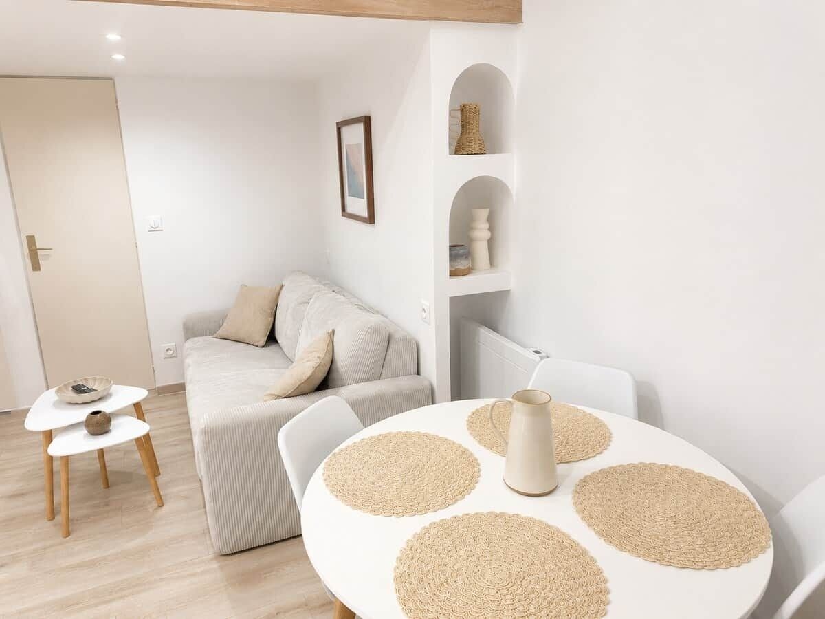 A minimalist living room with a sofa, a round table with placemats, a small side table, and a bookshelf.
