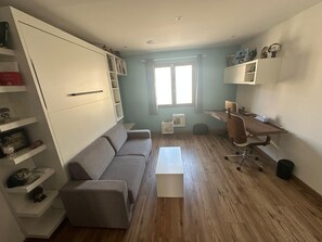 Ein kompakter Wohnraum mit einer Couch, einem Schreibtisch und Stauraumelementen.