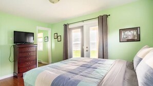 A bedroom with a bed, dresser, television, and a door leading to a balcony.