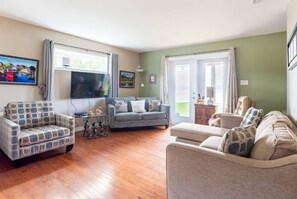 A living room with a sofa, armchairs, a television, and a window with curtains.
