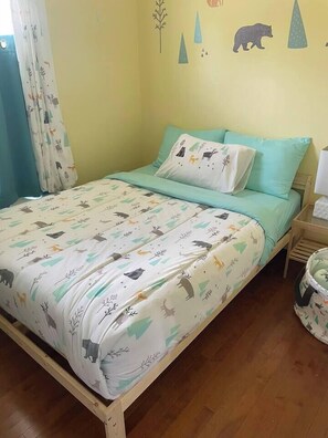 A bed with a patterned bedspread, a pillow, a bedside table with a lamp, and a wall with animal decals.