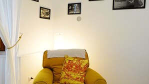Ein Zimmer mit einem gelben Sessel, einem weißen Vorhang und mehreren gerahmten Bildern an der Wand.