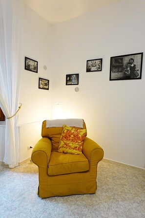Ein Zimmer mit einem gelben Sessel, einem weißen Vorhang und mehreren gerahmten Bildern an der Wand.