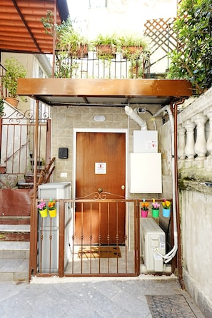 Ein verschlossener Eingang mit einer Holztür, einem weißen Verteilerkasten und Blumenkästen auf einem Balkon.