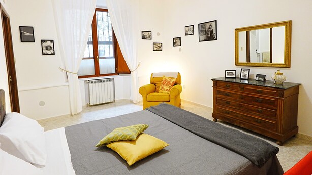 Ein Schlafzimmer mit Bett, Kommode, Stuhl und einem Fenster mit Vorhängen.