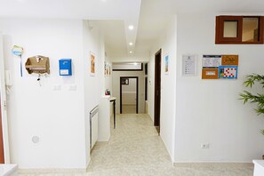 Un couloir d’hôtel avec un comptoir de réception, un coffre-fort bleu et des affiches d’information sur les mesures d’urgence accrochées aux murs.