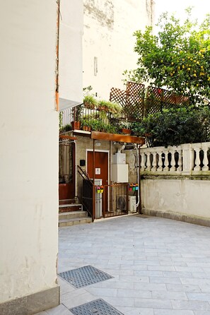 Une cour intérieure avec un escalier menant à une porte en bois, un portail en métal et un petit jardin agrémenté de plantes en pot.