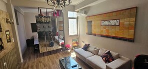 A living room with a sofa, a coffee table, a mirror, and a tiled wall with a sign. - Monastiraki Art House (Athina)