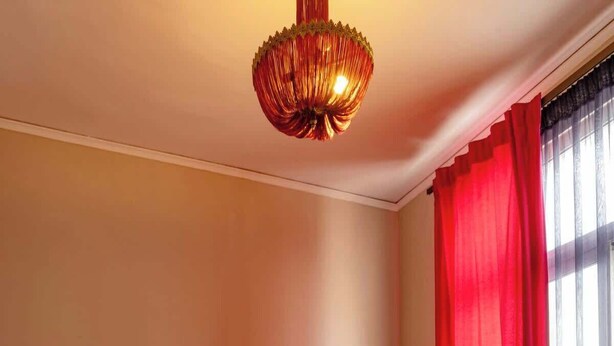 A hotel room with a bed, pillows, a bedside table, and a window with red curtains. - Monastiraki Art House (Athina)