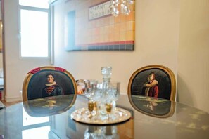 A dining table with two framed portraits, a crystal glass set, and a window with natural light. - Monastiraki Art House (Athina)