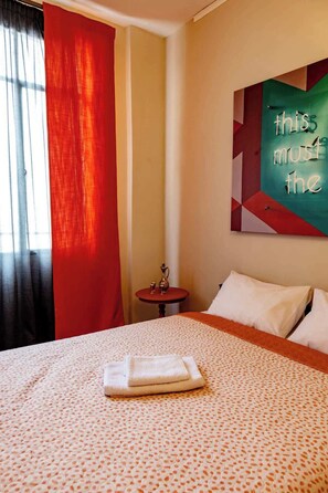 Een hotelkamer met een bed, een tafeltje, een decoratief object aan de muur en een raam met gordijnen.