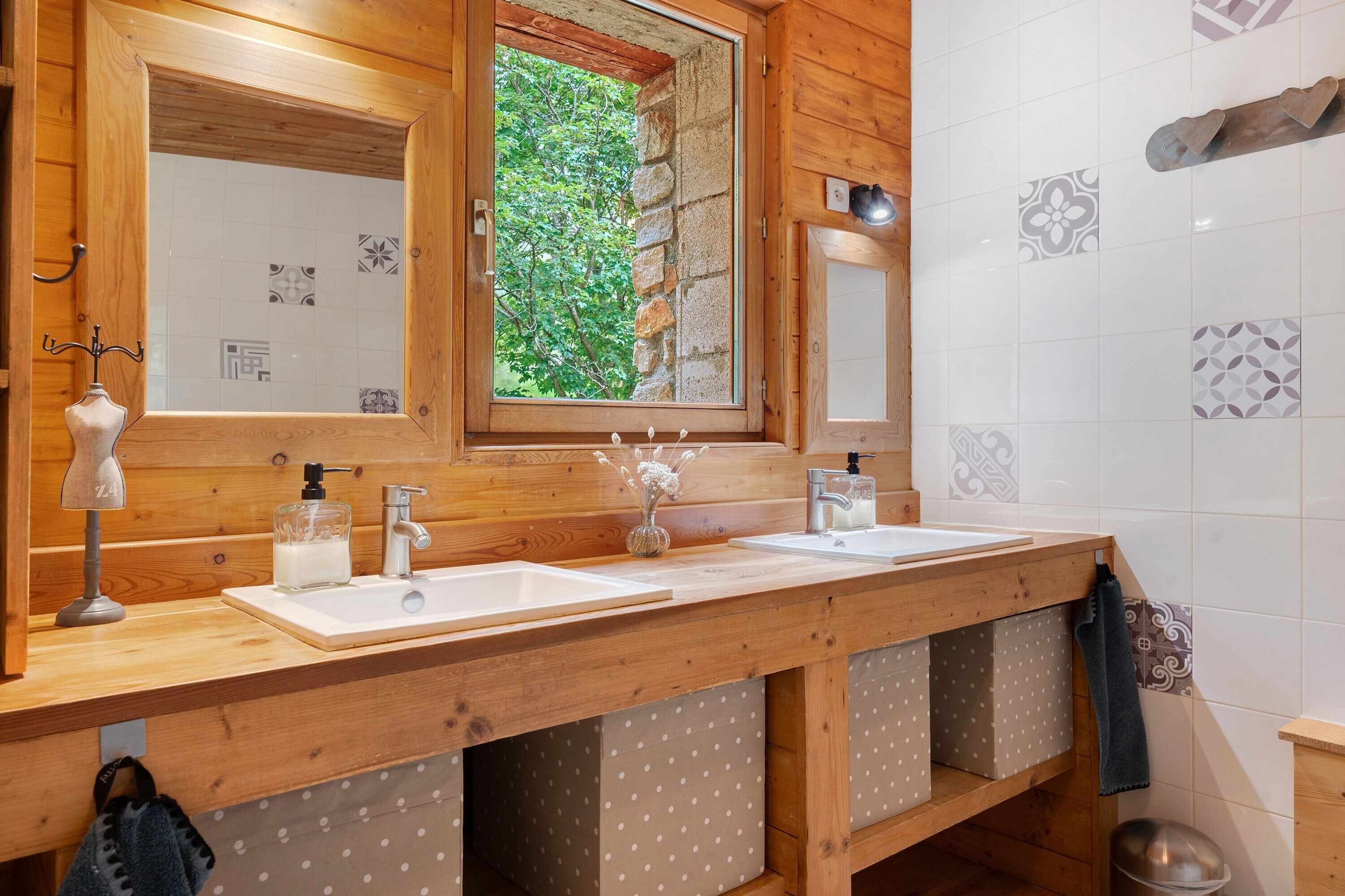A wooden bathroom with two sinks, a window with a view of greenery, and patterned tiles.