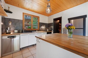 Cocina moderna con techo de madera, electrodomésticos de acero inoxidable y un ventanal con vistas a un jardín.