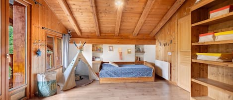 Ein Holzinnenraum mit einem Bett, einem Regal mit Aufbewahrungsboxen und einem Fenster mit Vorhängen.