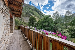 Eine Holzterrasse mit einer Steinmauer, die auf eine gebirgige Landschaft mit blühenden Pflanzen blickt.