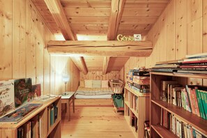 Ein gemütliches Zimmer mit Holzwänden und -decke, einem Bett mit Steppdecke, einem kleinen Tisch mit Büchern und einem Bücherregal voller Bücher.